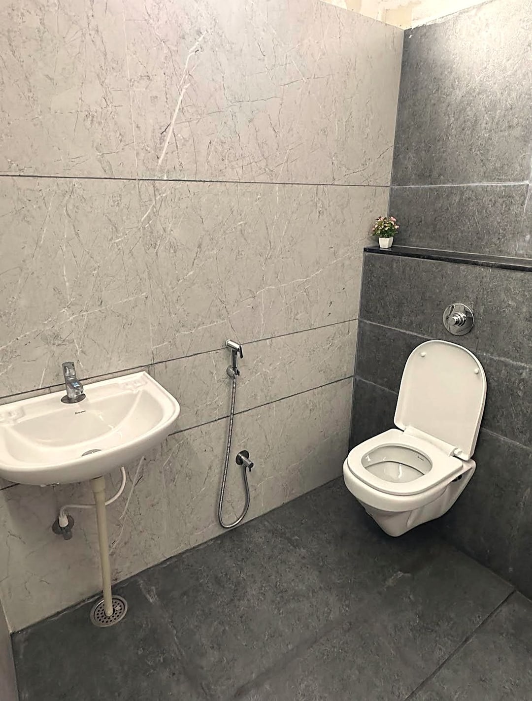 The shared bathroom used by the dormitory at Cibara Comforts, with a washbasin, western toilet and grey tiling