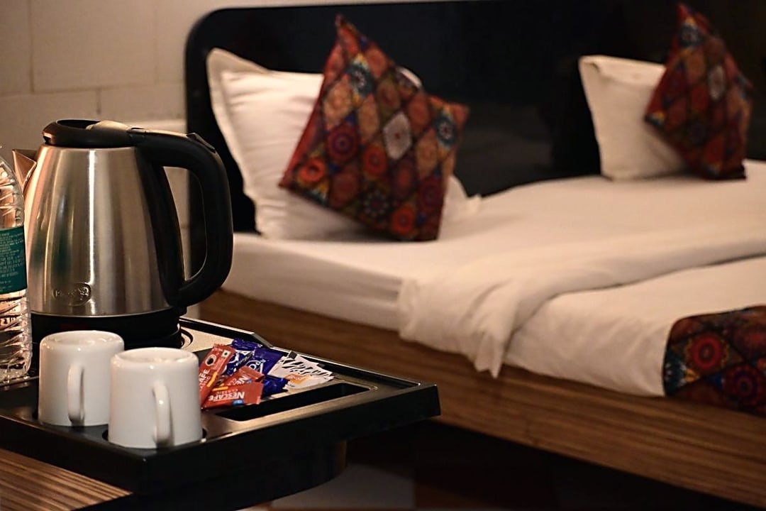 An electric kettle, two cups and a complimentary tea tray set out beside the bed in a Premium room at Cibara Comforts