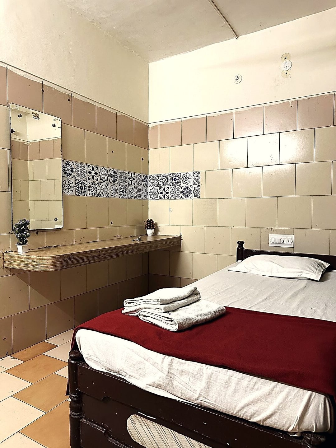 Single room showing the washbasin, mirror and a patterned tile band along the wall